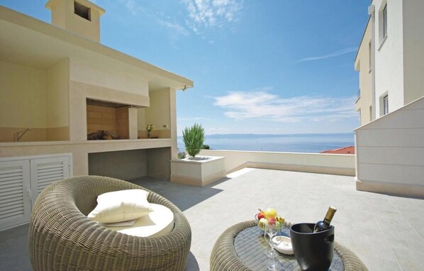 A balcony with wicker furniture, a small table with a drink, and a view of the sea.