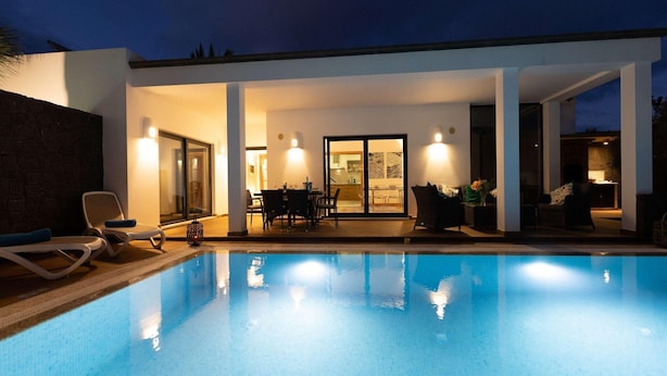 Een moderne buitenzwembadzone met een overdekt terras, lounge fauteuils en een eettafel.