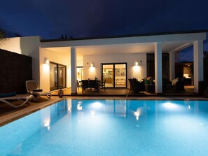A modern outdoor pool area with a covered patio, lounge chairs, and a dining table. - Private Pool in Playa Blanca (Playa Blanca)