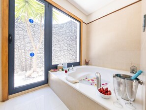 A modern bathroom with a large bathtub, a window with a view of a rocky landscape, and a small balcony area. - Private Pool in Playa Blanca (Playa Blanca)