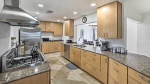 Eine moderne Küche mit Edelstahlgeräten, Holzschränken und Granit Arbeitsplatten. An der Wand hängt eine Uhr.
