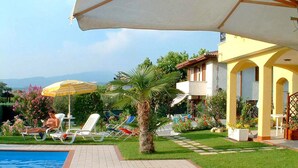 Un espace piscine avec des chaises longues et des parasols, une pelouse bien entretenue et un bâtiment doté d’un balcon.