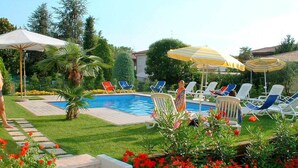 A swimming pool with lounge chairs and umbrellas, surrounded by a well-maintained garden with flowers and a stone pathway.