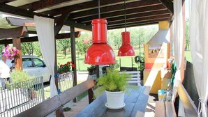An outdoor patio with wooden benches, red hanging lamps, and a white planter with greenery.