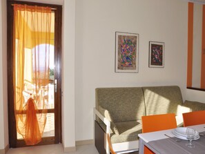A room with a sofa, two framed artworks, a dining table with chairs, and a window with sheer curtains. - Holiday Home in Lazise near Lake Garda (Lazise)