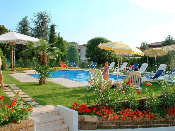 A swimming pool with lounge chairs and umbrellas, surrounded by a well-maintained garden with flowers and a stone pathway.
