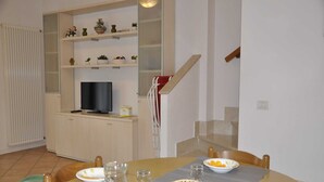 A dining area with a table set for two, a television, and a kitchen area with cabinets and shelves.