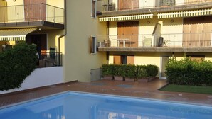 A swimming pool with a tiled deck, surrounded by potted plants and a building with balconies.