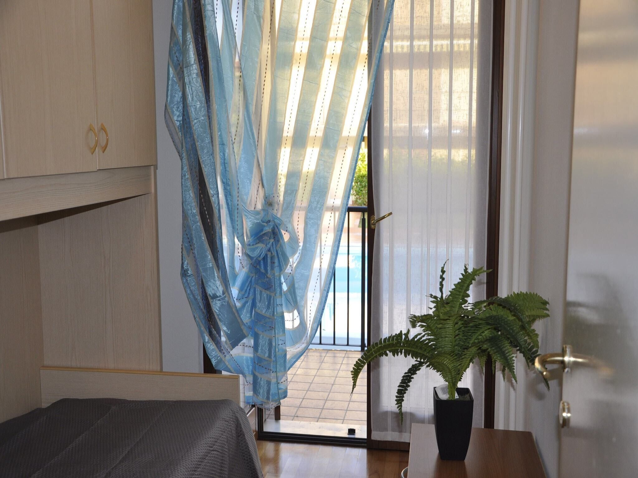 A bedroom with a bed, a potted plant, a window with a curtain, and a door.