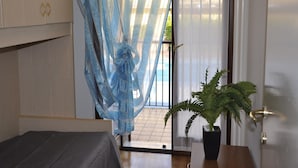 A bedroom with a bed, a potted plant, a window with a curtain, and a door.