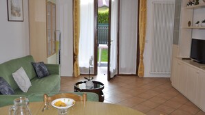 A living room with a green sofa, a dining table with a bowl of fruit, and a television on a cabinet.