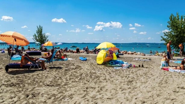 A beach with umbrellas, lounge chairs, and people sunbathing.