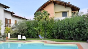 A swimming pool with lounge chairs, surrounded by dense greenery and a building with balconies.