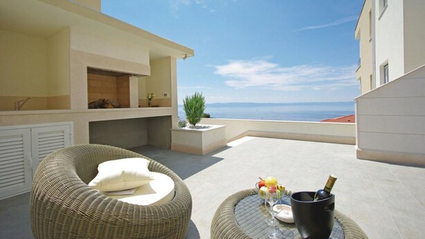Un balcon agrémenté de meubles en osier, une petite table avec une bouteille et des verres, et une vue sur la mer.