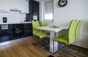 Una cocina moderna con armarios blancos, un horno negro y sillas verdes alrededor de una mesa blanca.