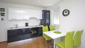Une cuisine moderne avec des meubles blancs, un plan de travail noir et un coin repas comprenant une table blanche et des chaises vertes.