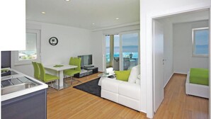 Un salon moderne avec un canapé blanc, des fauteuils verts, une table à manger et un téléviseur.