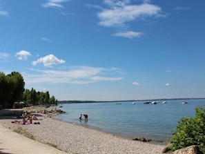 A pebbled beach with people sunbathing, a calm lake, and boats in the distance. - Apartment in Lazise near Lake Garda (Lazise)