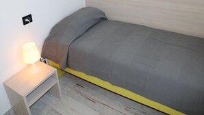 Un lit simple avec une tête de lit en bois, une table de chevet avec une lampe et une prise électrique sur le mur.