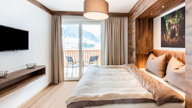 Une chambre dotée d’un grand lit, d’un téléviseur fixé au mur, d’un balcon avec des chaises et offrant une vue sur la montagne.