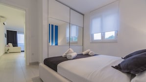 Ein modernes Schlafzimmer mit einem großen Bett, einem Spiegel und Blick auf den angrenzenden Raum.