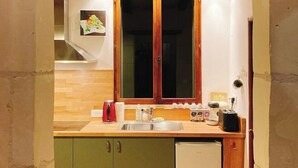 Een compacte keuken met houten balken, een spoelbak, een kleine koelkast en een raam met een afbeelding aan de muur.