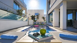Un espace piscine extérieur moderne, avec des chaises longues, un livre, des lunettes de soleil et une pomme.