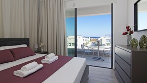 Une chambre d’hôtel avec un grand lit, un balcon doté d’une table et de chaises, et une vue sur le paysage urbain.
