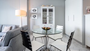 Un'area pranzo moderna con un tavolo in vetro, sedie bianche, un divano grigio e un armadietto bianco con ante in vetro.