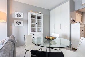 Een moderne keuken met een glazen eettafel, witte keukenkastjes en een schaal met fruit.