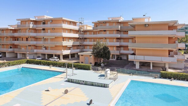En høj beboelsesejendom med altaner, swimmingpool og en overdækket terrasse.