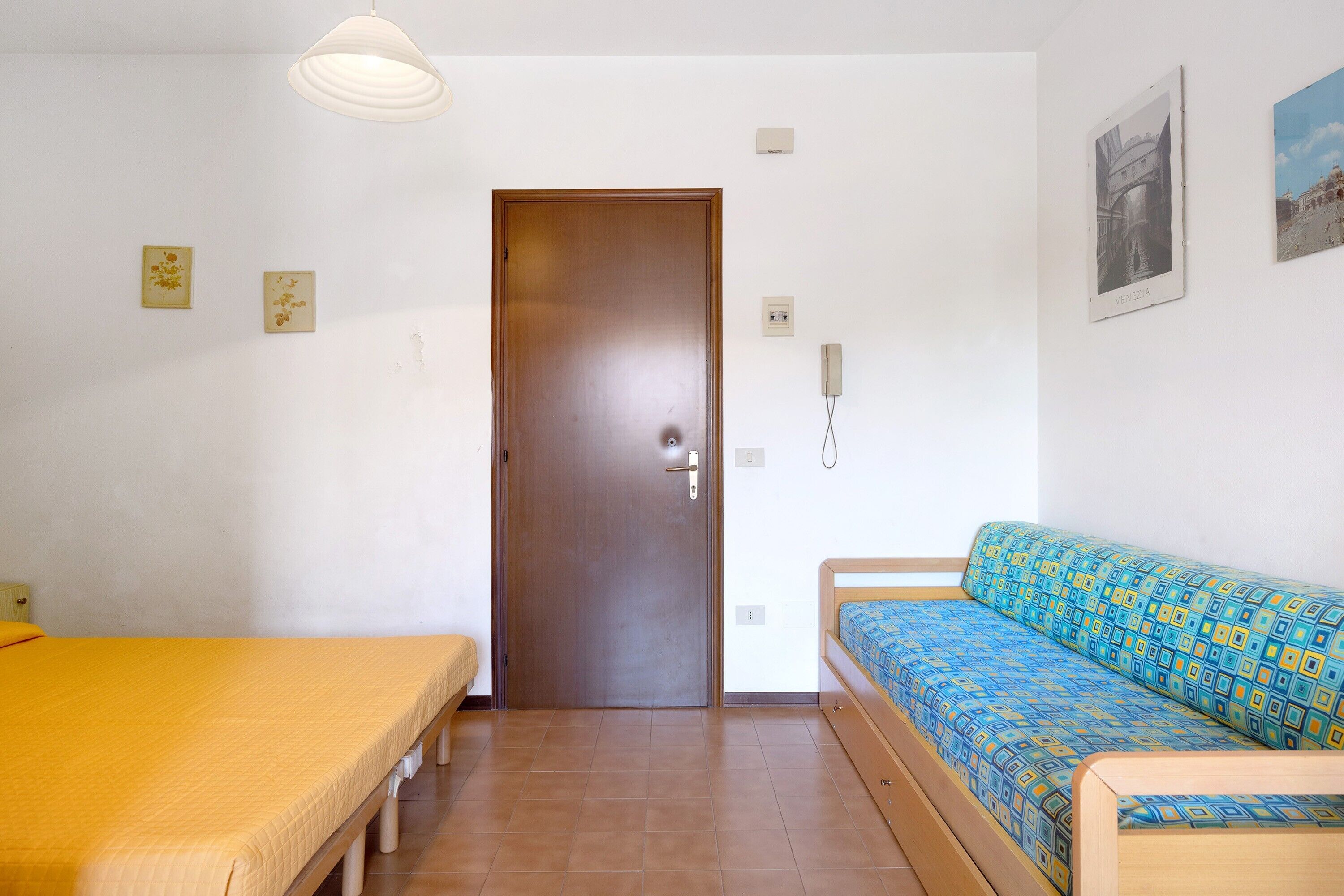 A room with a bed, a sofa, a door, and a wall-mounted phone.