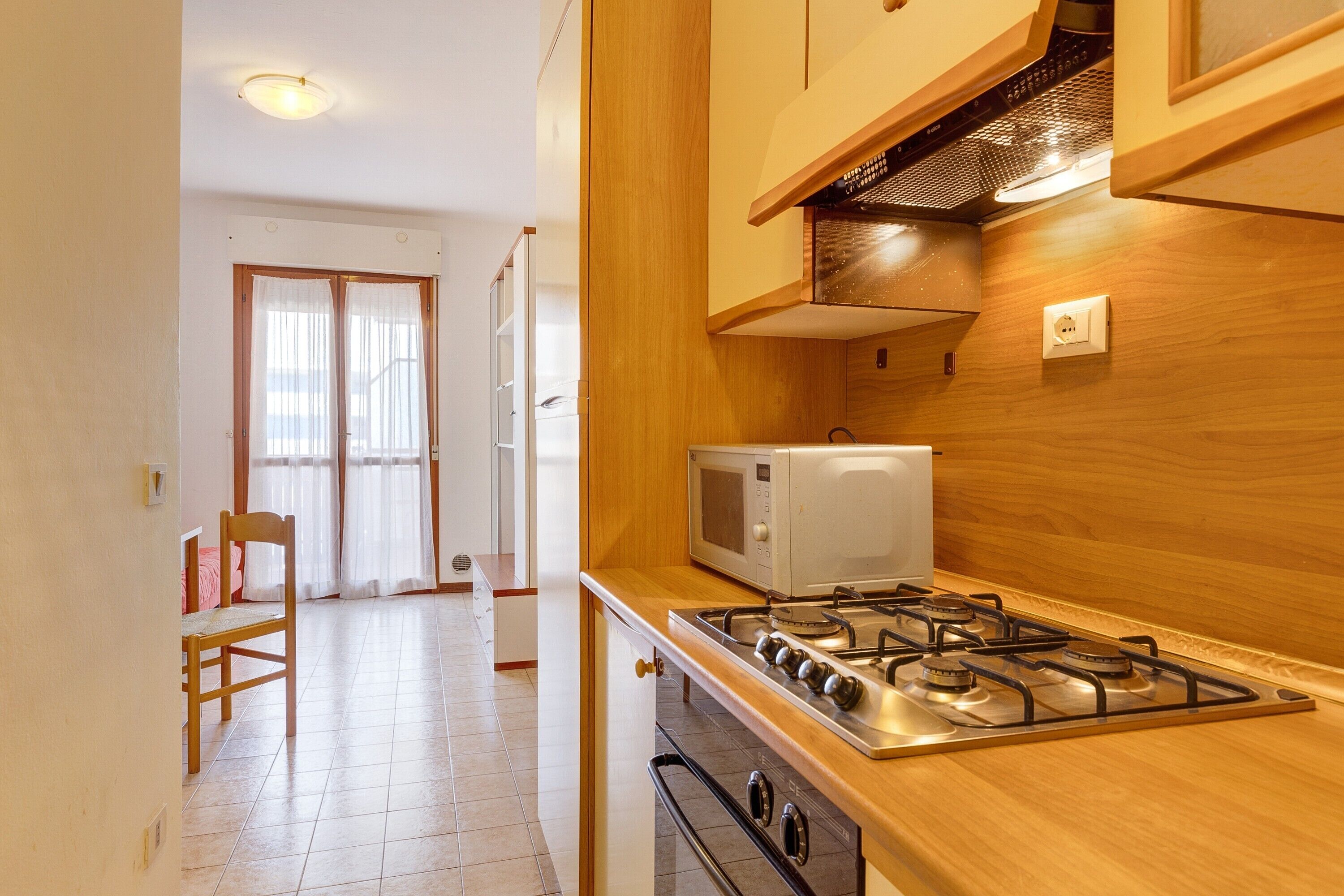 A kitchen with a gas stove, microwave, wooden cabinets, and a window with curtains.