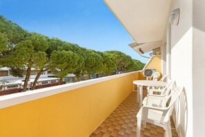Un balcon avec un mur jaune, des chaises blanches, une petite table et une vue sur les arbres et les bâtiments.