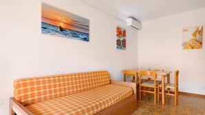 A room with a checkered sofa, a dining table with chairs, and wall art depicting a sunset and food. - Apartment "Condominio Simma 1B6" with A/C & Terrace (Bibione)