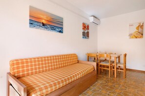 Una stanza con un divano a quadri, un tavolo da pranzo con sedie e opere d'arte raffiguranti un tramonto e cibo.