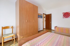 Une chambre à coucher avec une armoire en bois, une chaise, un tapis coloré et un lit recouvert d’une couvre-lit à motifs.
