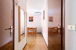 Un couloir avec une porte en bois, une table à manger avec des chaises et un climatiseur fixé au mur.