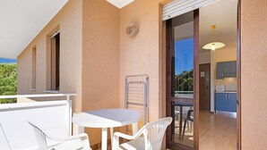 A balcony with a table and chairs, a sliding glass door leading to a kitchen, and a view of greenery.