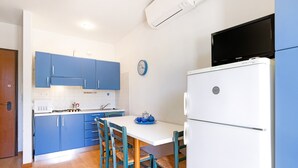 A kitchen with blue cabinets, a white refrigerator, a dining table with chairs, and a clock on the wall.