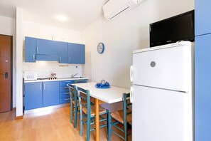 A kitchen with blue cabinets, a white refrigerator, a dining table with chairs, and a clock on the wall.