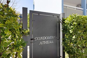 A metal gate with 'CONDOMINIO ATHENA' written on it, surrounded by greenery.