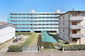 Un edificio a più piani con tetto piatto, un campo da tennis di fronte e una barca parcheggiata all'esterno.