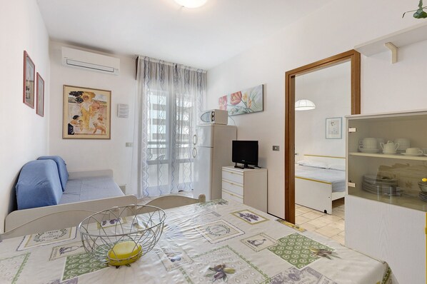 A compact room with a bed, a small desk, a television, and a cabinet with dishes.