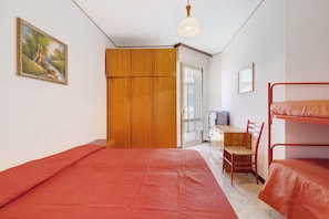 A room with a bunk bed, a wooden wardrobe, a desk with a chair, and a painting on the wall.