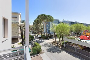 Une rue résidentielle bordée de bâtiments modernes, avec une aire de jeux et un chemin piétonnier ombragé par des arbres.