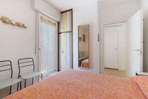 Une chambre à coucher avec un lit, deux chaises, une table, un miroir et une porte.