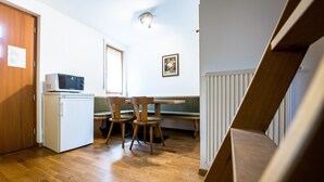 A compact kitchen with a microwave, a small refrigerator, a wooden dining table with chairs, and a bench. - Apartment 'Issingerhof 1' with Mountain Views, Garden & Wi-Fi (Campo di Tures)