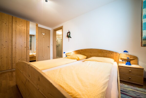 Una cama de madera con dos almohadas, una mesita de noche con una lámpara y un espejo en la pared.