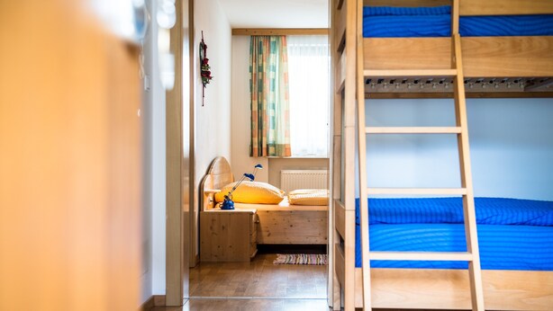 A bunk bed room with a ladder, a desk with a lamp, and a window with curtains. - Apartment 'Issingerhof 1' with Mountain Views, Garden & Wi-Fi (Campo di Tures)